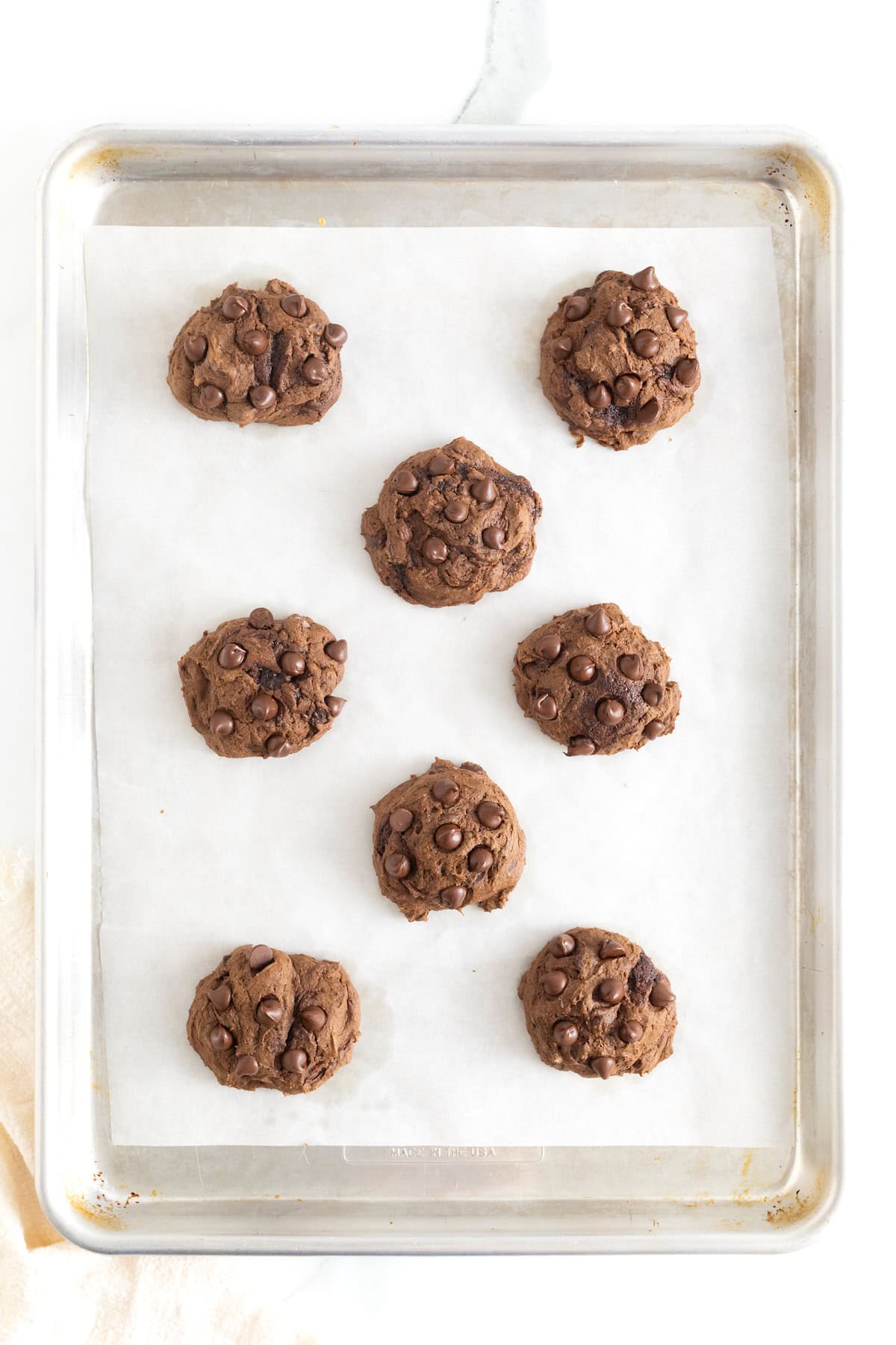 Eight triple chocolate pumpkin cookies on a parchment lined baking sheet.