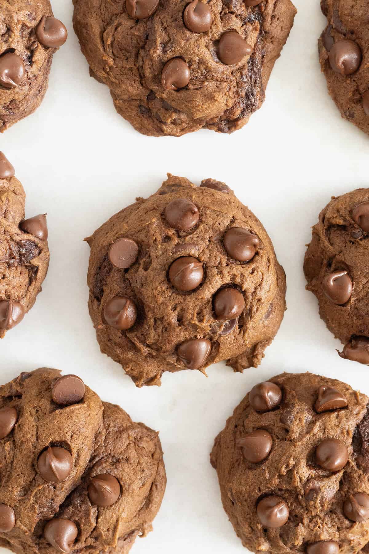Eight triple chocolate pumpkin cookies on a parchment lined baking sheet.