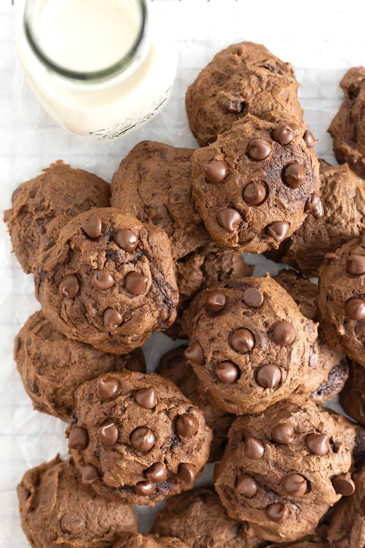 A pile of triple chocolate cookies on a parchment lined metal cooling rack.