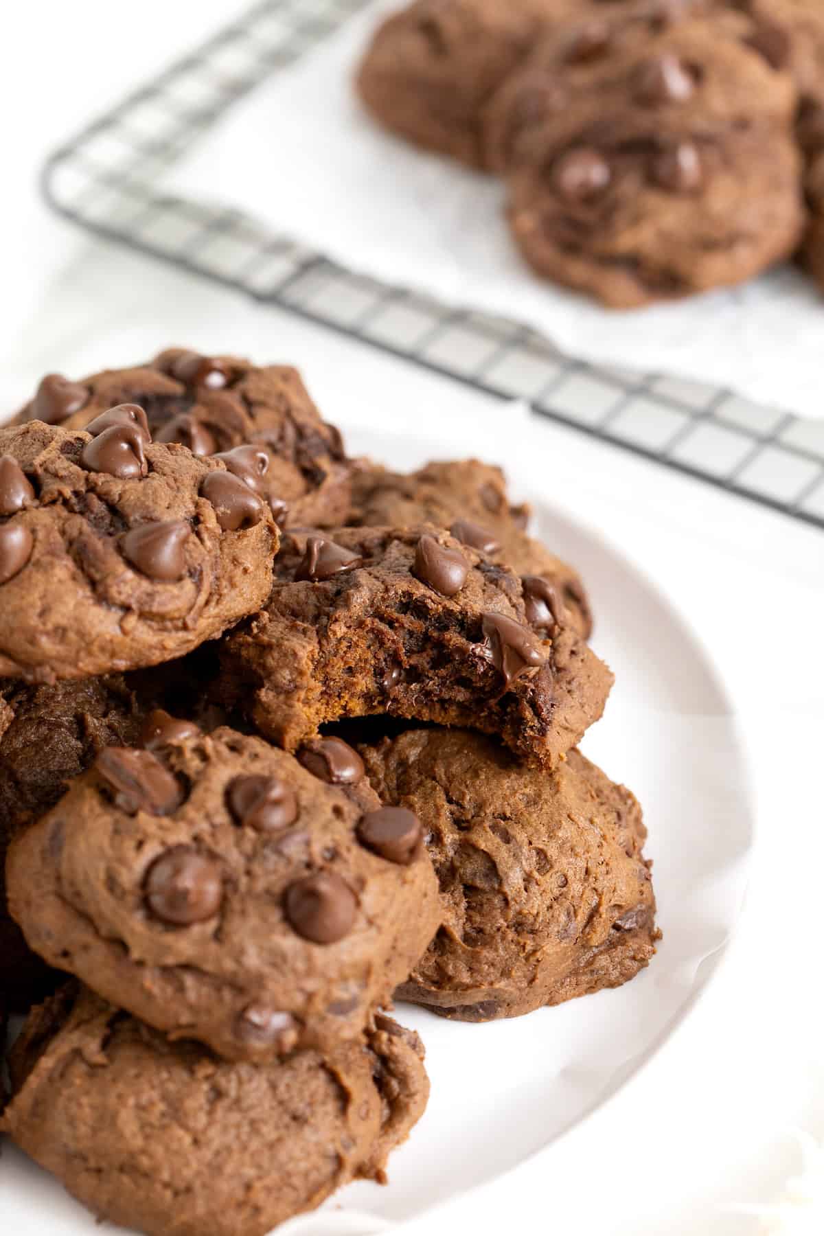 A plate of triple chocolate cookies on a white surface. One of the cookies has a bite out of it.