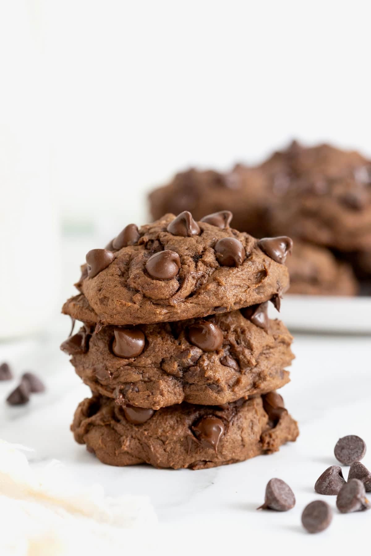 A stack of three triple chocolate pumpkin cookies on a white marble counter. There is a plate of cookies in the background.