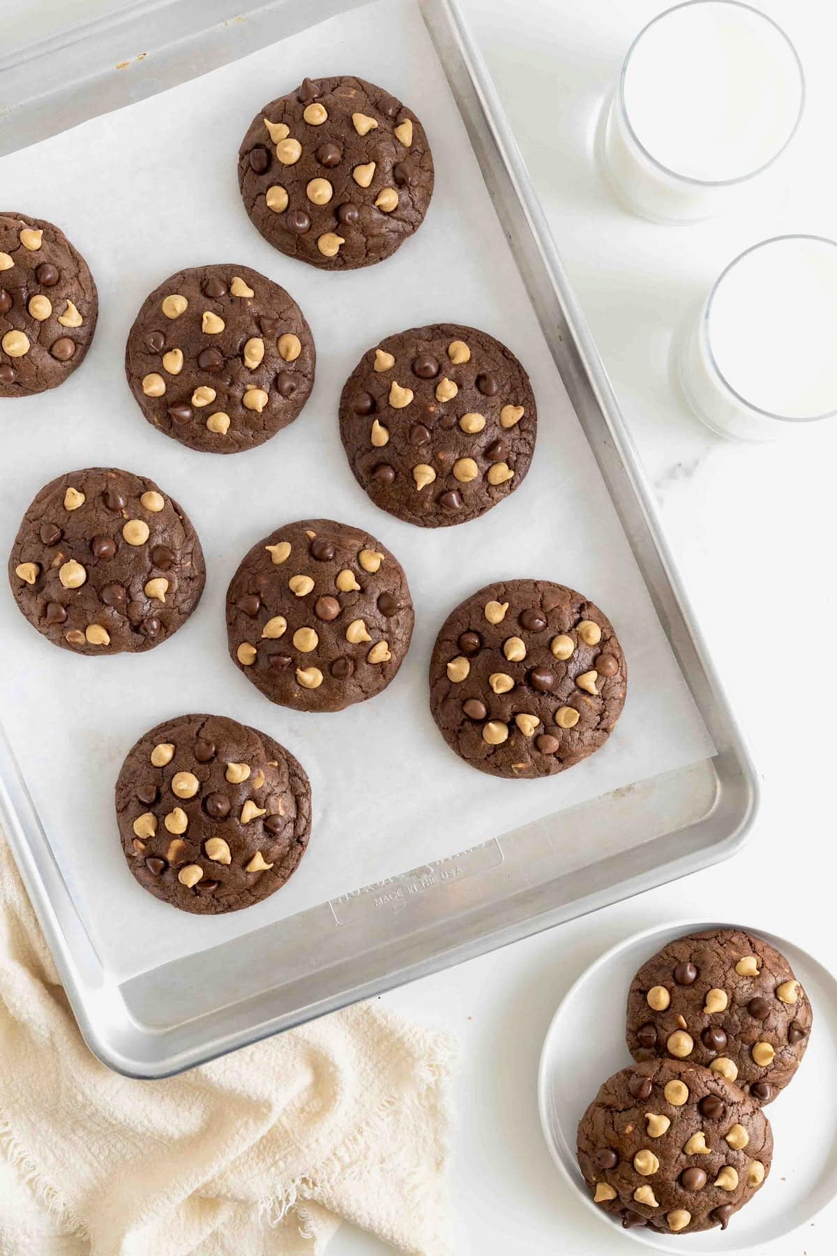 Eight chocolate cookies with peanut butter chips on a parchment lined aluminum baking sheet.
