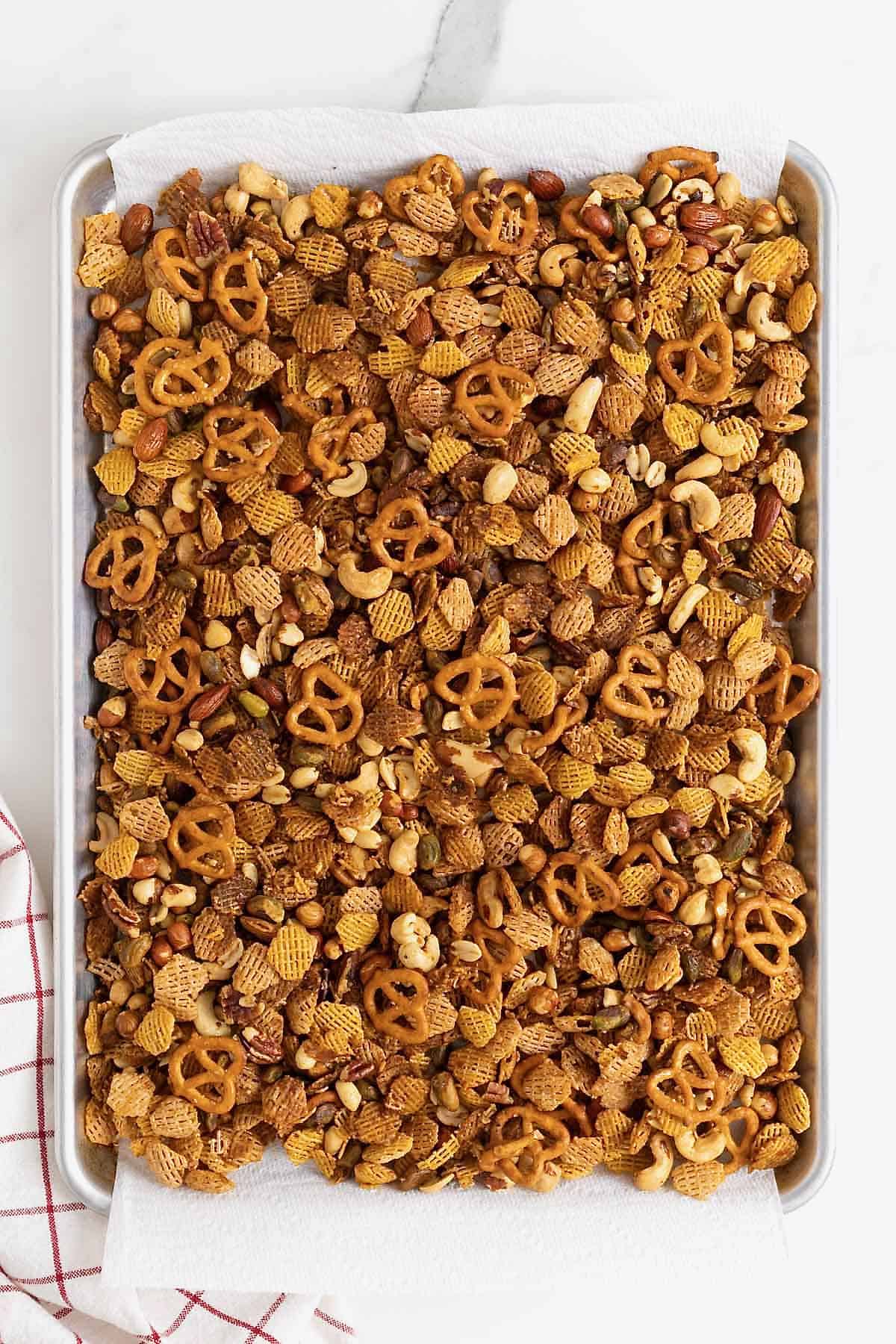 Snack mix on paper towels on an aluminum baking sheet.