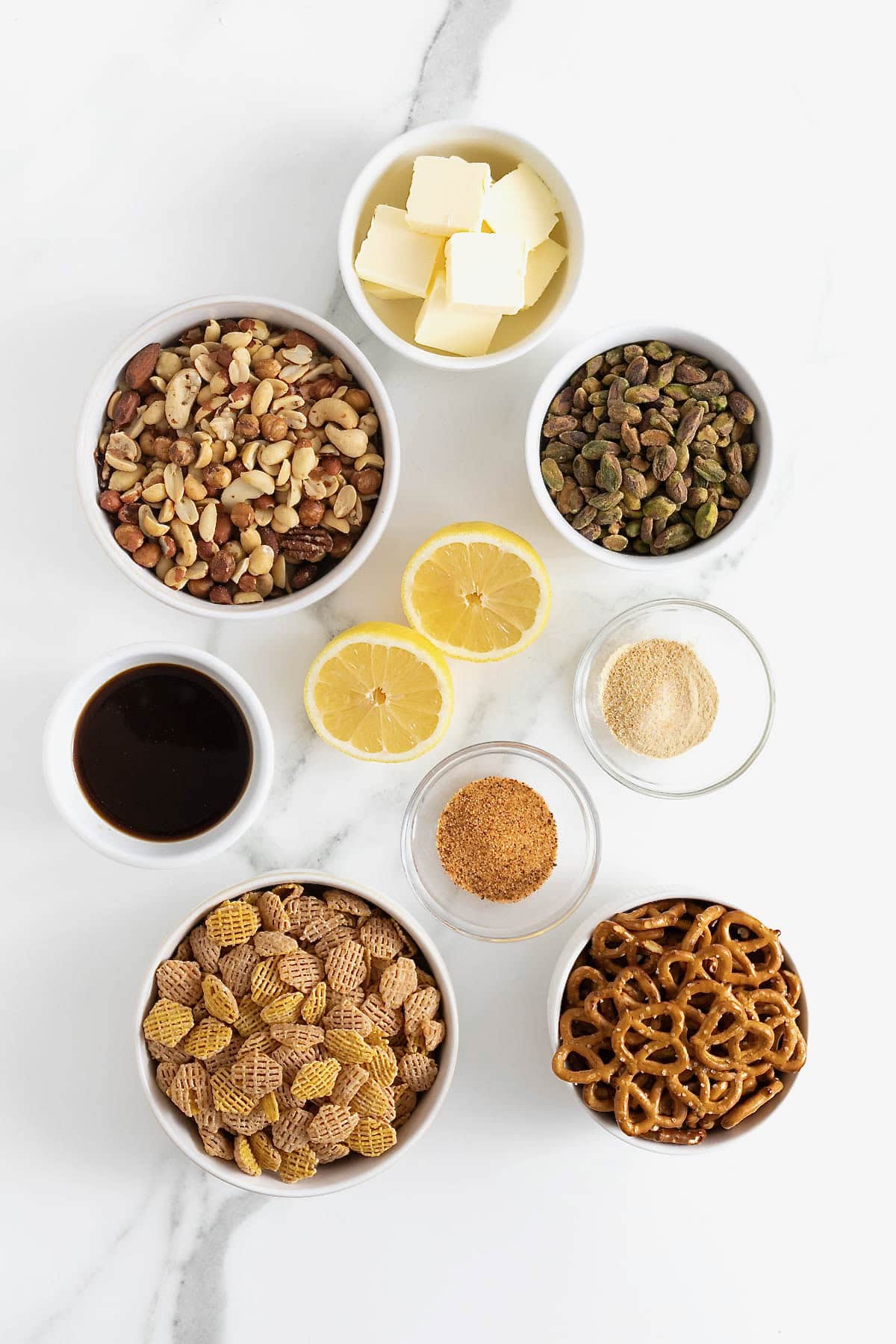 Ingredients to make SuSu's Cereal Snack Mix in small glass dishes on a white marble counter.