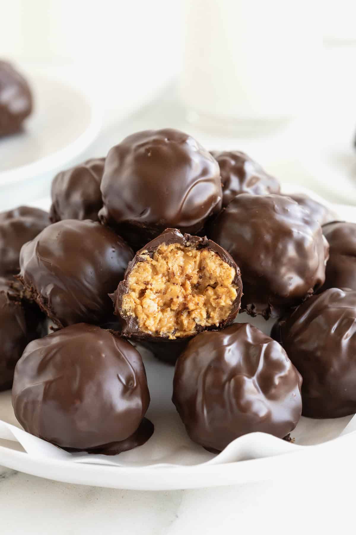 A pile of dark chocolate peanut butter balls in a parchment lined white serving dish.