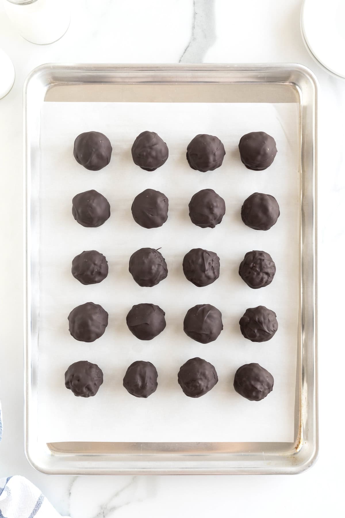 20 Chocolate covered peanut butter balls on a parchment lined rimmed baking sheet.