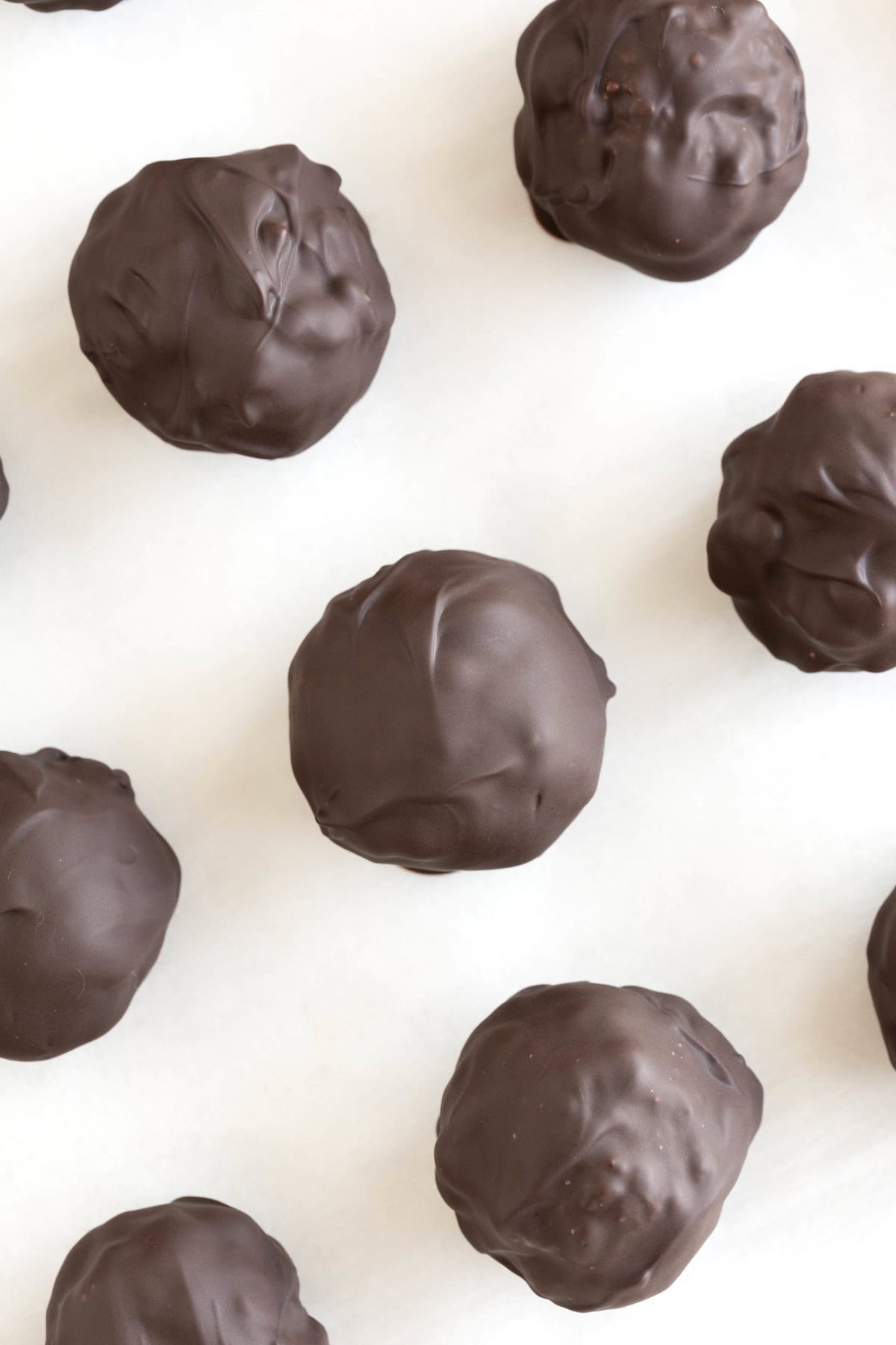 Seven dark chocolate peanut butter balls on a piece of parchment.