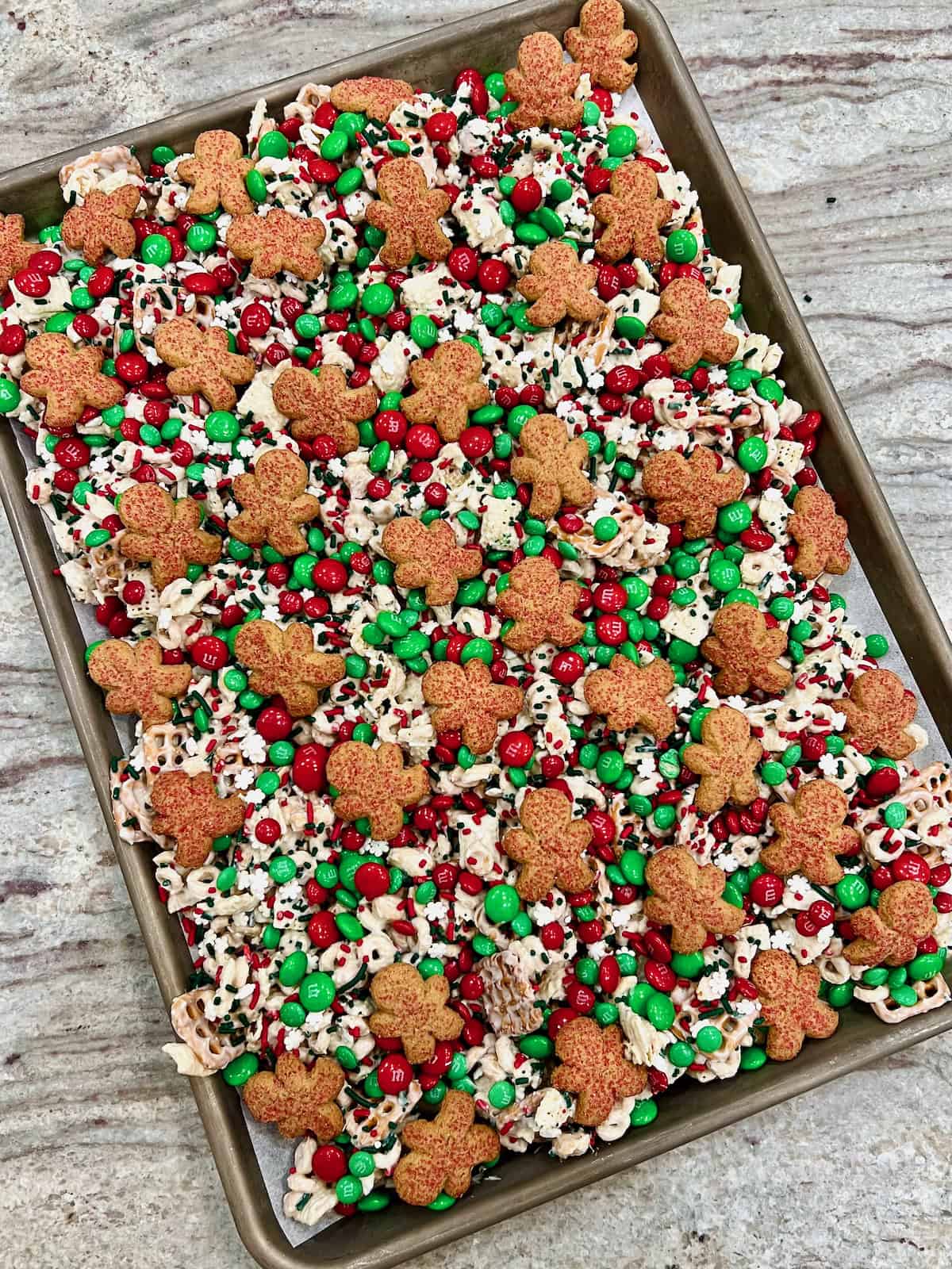 A sheet pan of Christmas Crunch Mix on a gray marble counter.