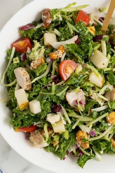 A large white bowl of green salad with cut up tomatoes, shredded cheese and chunks of chicken.