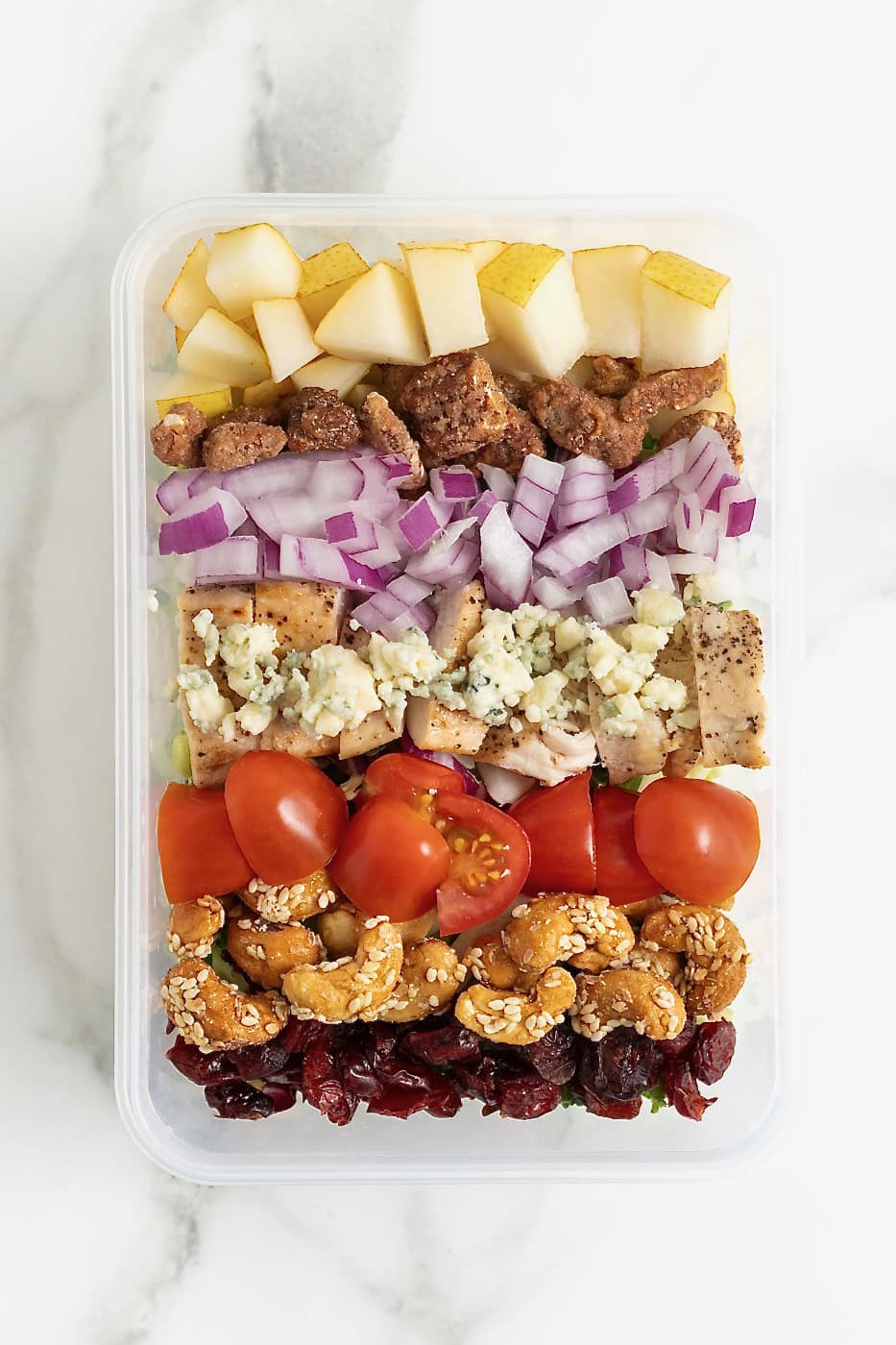 Apples, onions, gorgonzola crumbles, cherry tomato halves, candied cashews and dried cranberries in an airtight plastic container.