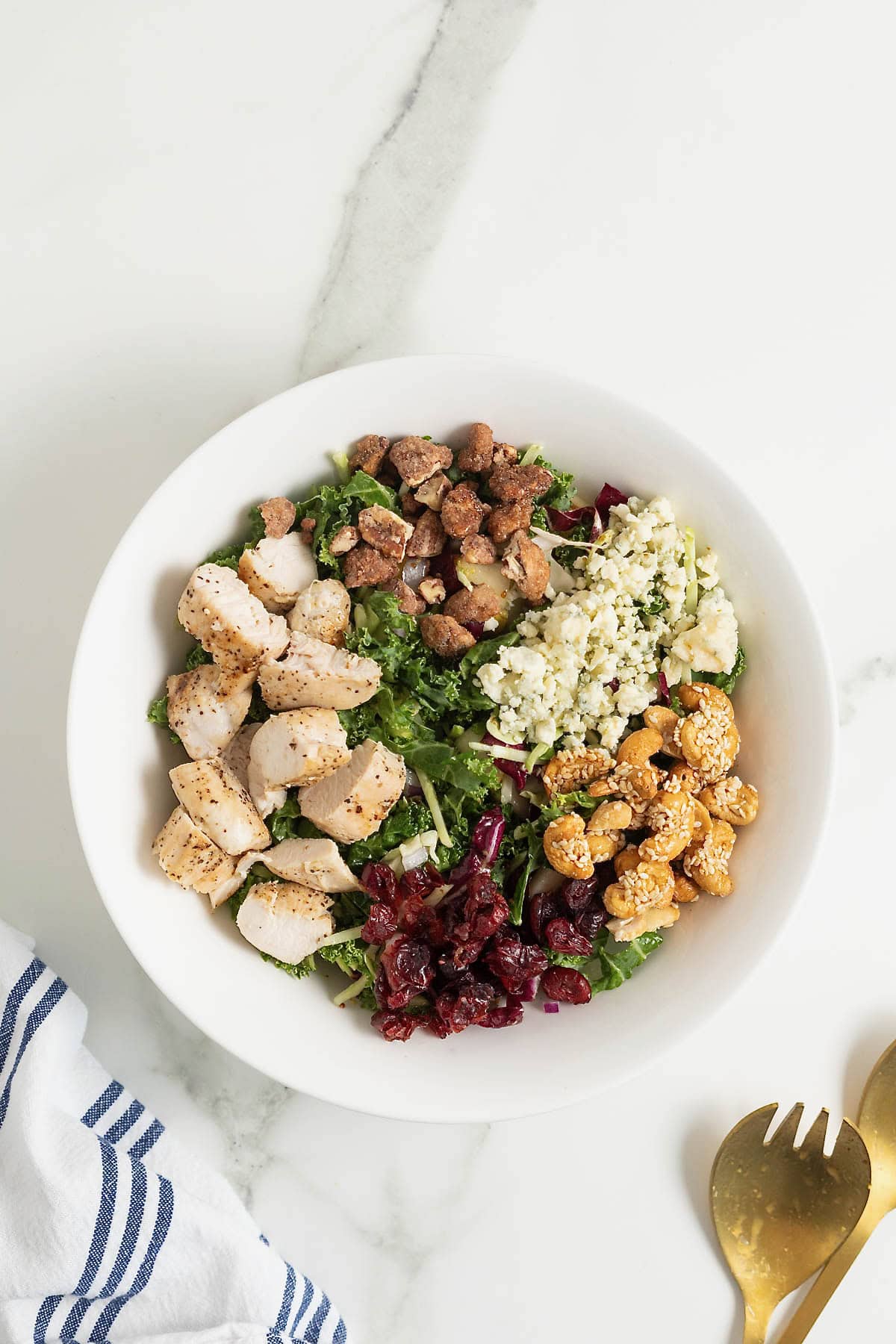 Chunks of chicken, walnuts, cheese, and cranberries added to a salad in a white bowl.