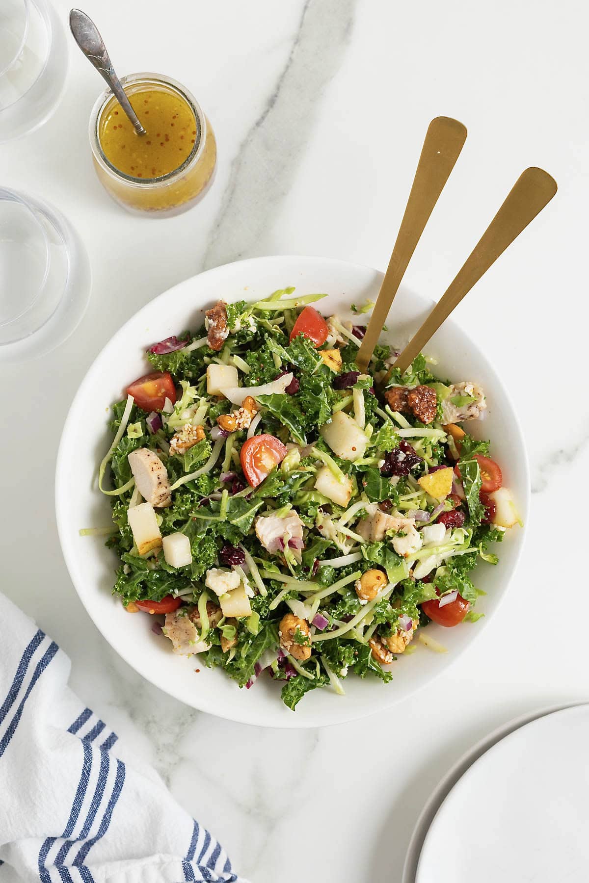 A large white bowl of green salad with cut up tomatoes, shredded cheese and chunks of chicken.
