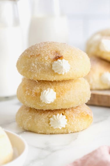 A stack of three cream filled baked donuts on a white surface.