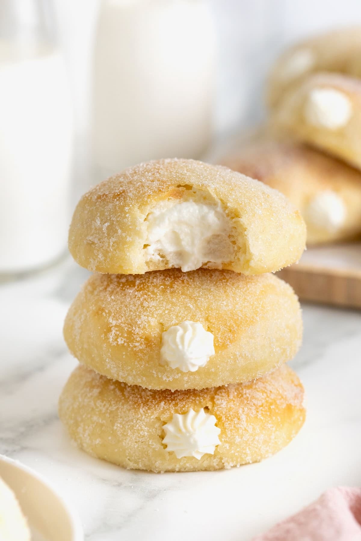 A stack of three cream filled baked donuts on a white surface. The top donut has a bite out of it.