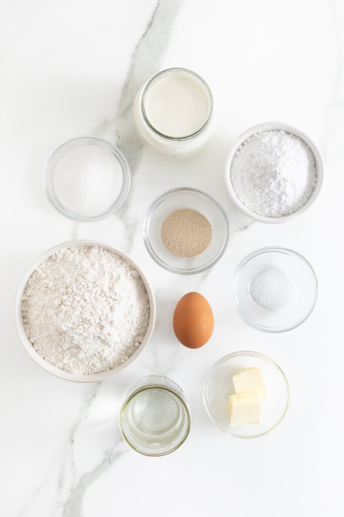 Ingredients to make cream filled baked donuts in small glass dishes on a white marble counter.