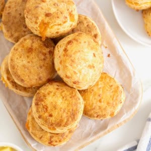 A pile of cheddar biscuits on non oblong cutting board covered in parchment.