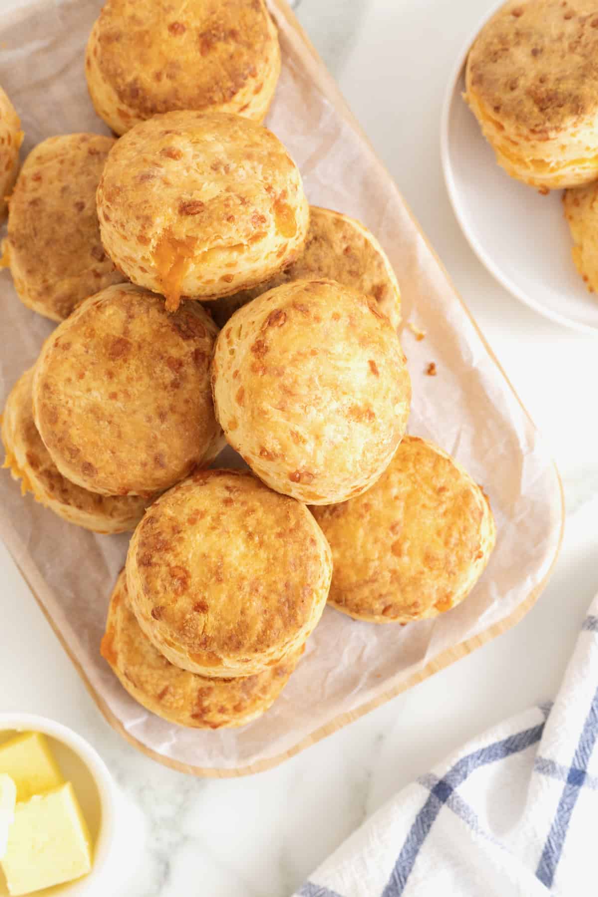 A pile of cheddar biscuits on non oblong cutting board covered in parchment.