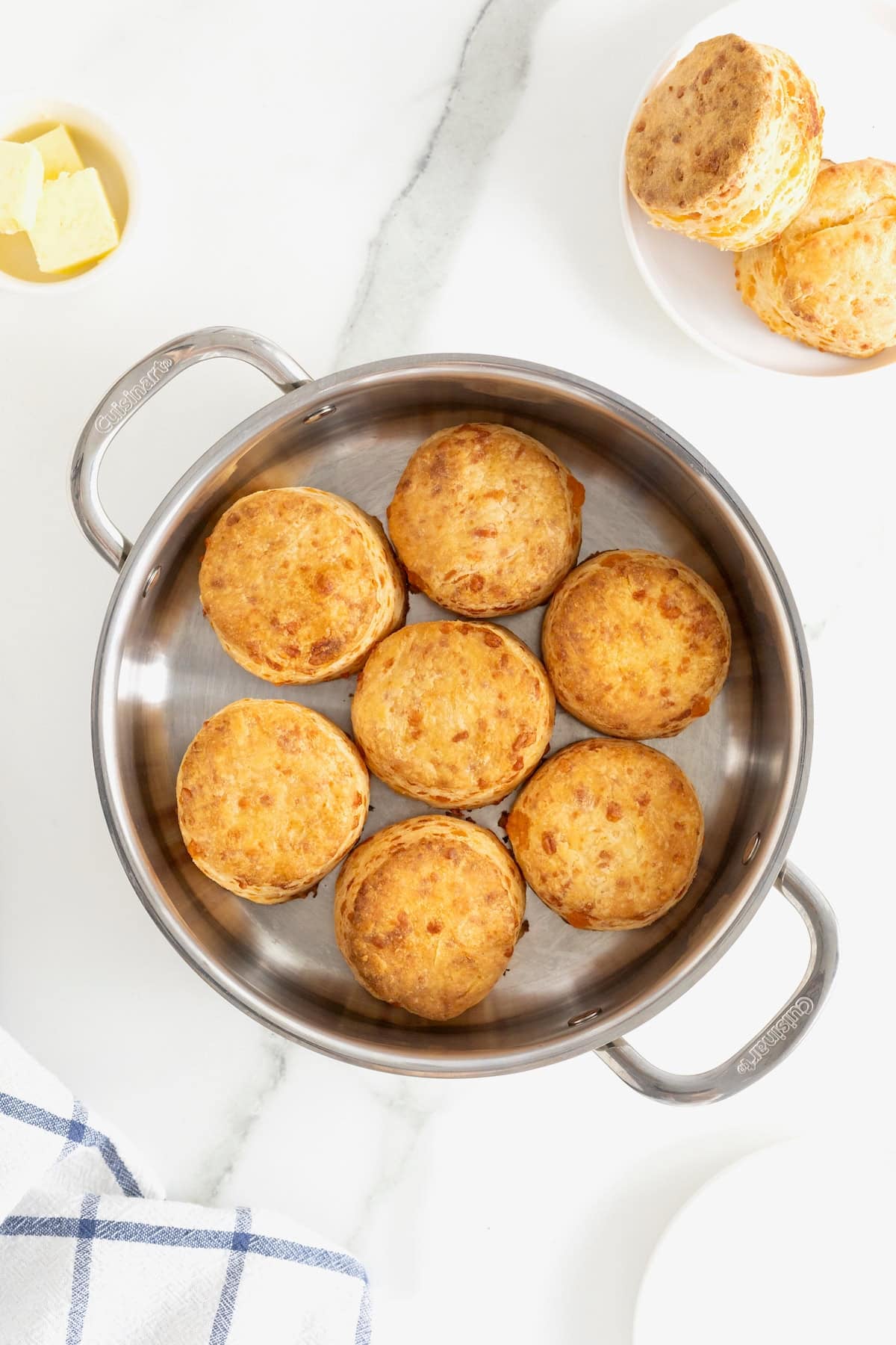 A stainless steel oven-safe skillet with seven cheddar biscuits in it.