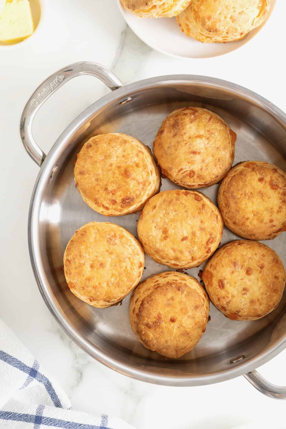 A stainless steel oven-safe skillet with seven cheddar biscuits in it.