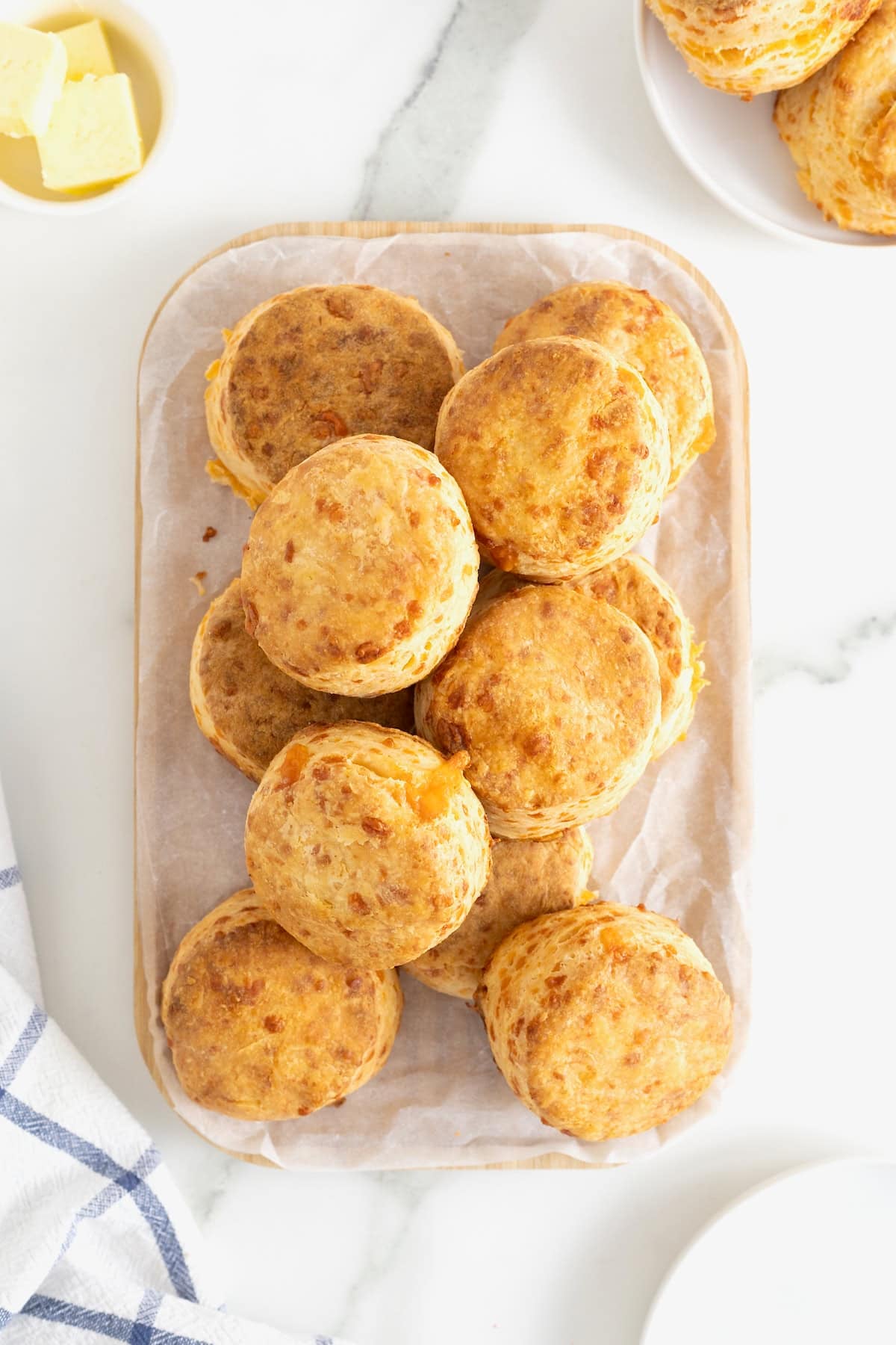 A pile of cheddar biscuits on non oblong cutting board covered in parchment.