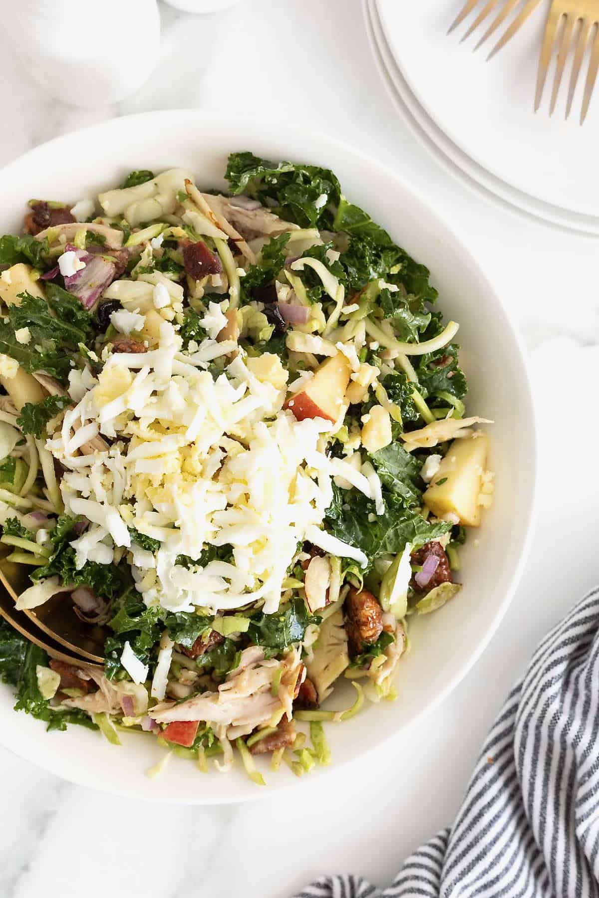 A kale and roasted chicken salad with chopped pecans in a large white serving bowl.