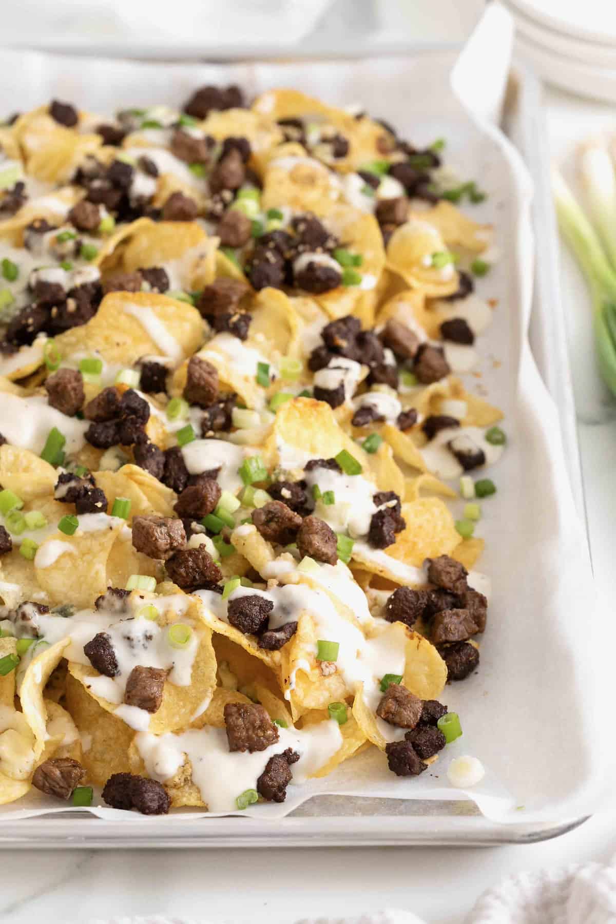 Steak and Blue Cheese Nachos on a parchment lined baking sheet.