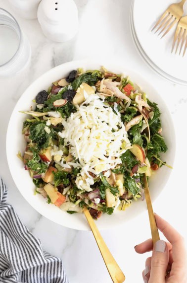 A kale and roasted chicken salad with chopped pecans in a large white serving bowl.