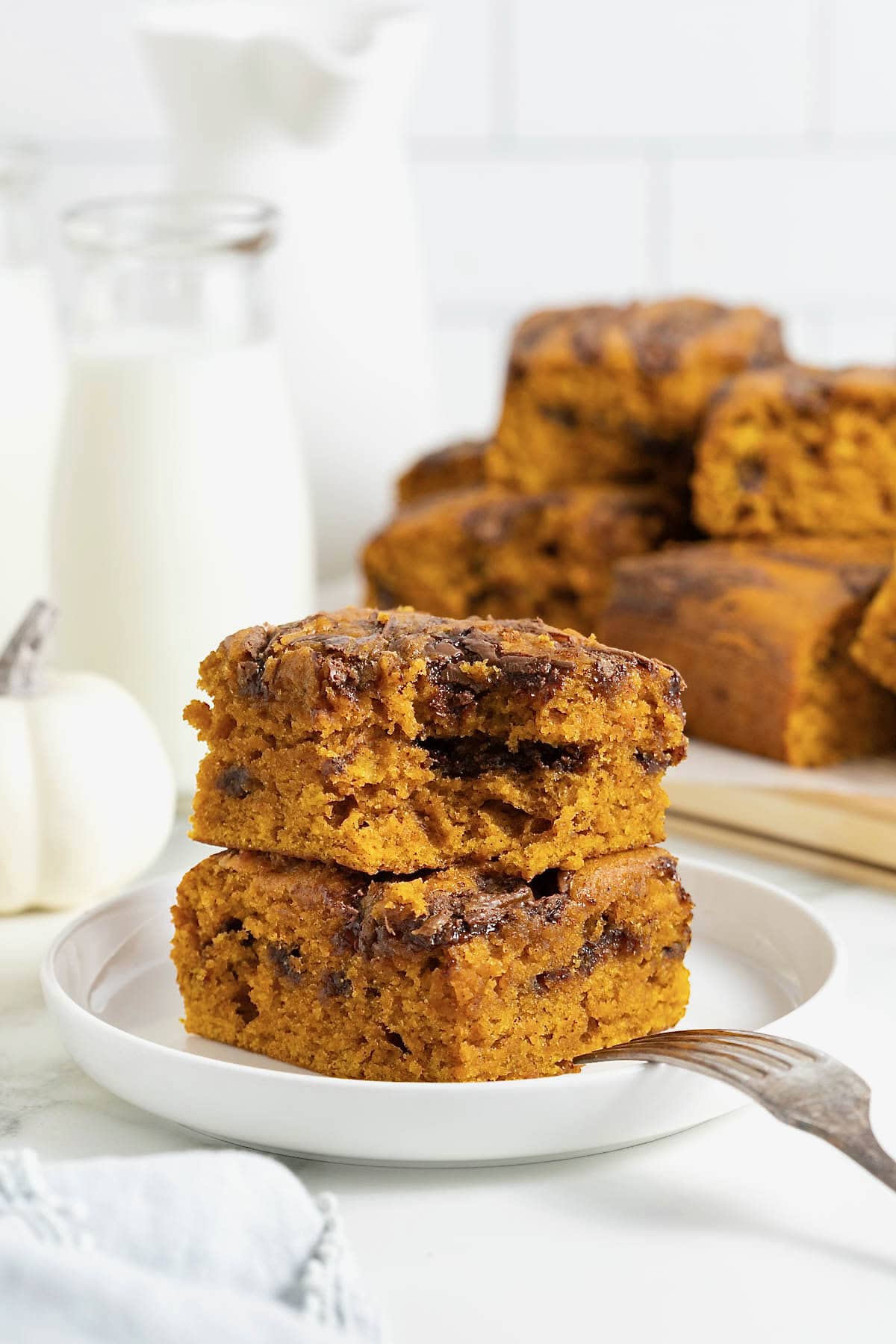 A stack of two pumpkin Nutella cake bars on a white rimmed plate. There is a bite out of the top bar and a fork resting on the edge of the plate.