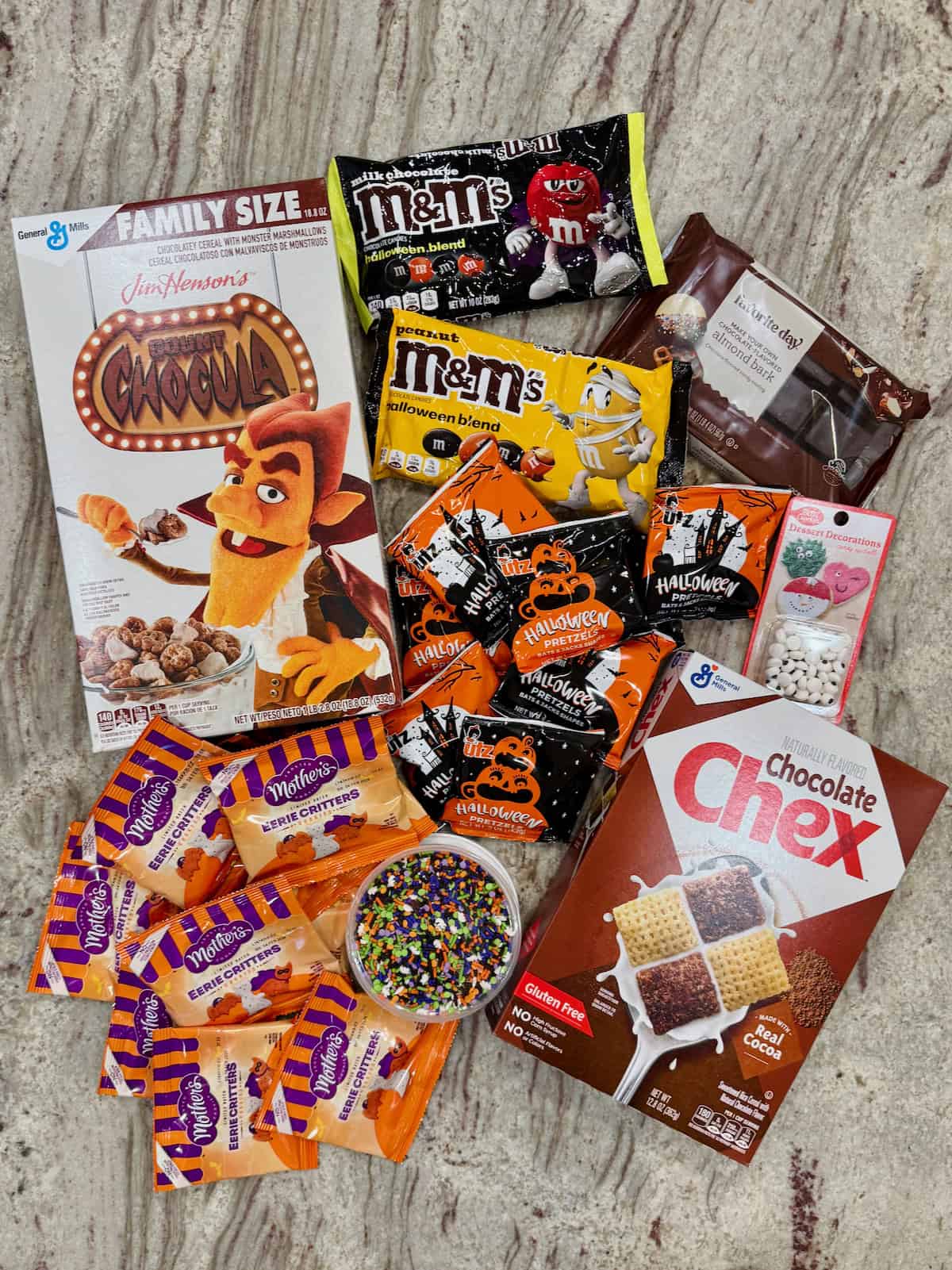 Ingredients to make spooky snack mix on a gray marble counter.