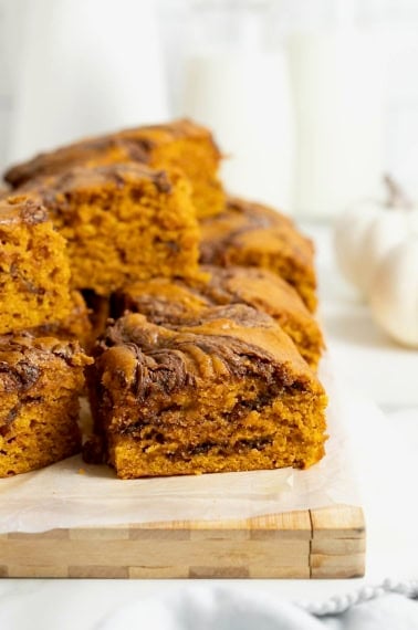 A pile of Nutella Swirled Pumpkin Cake Bars on a parchment lined wooden cutting board.