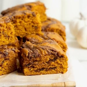 A pile of Nutella Swirled Pumpkin Cake Bars on a parchment lined wooden cutting board.
