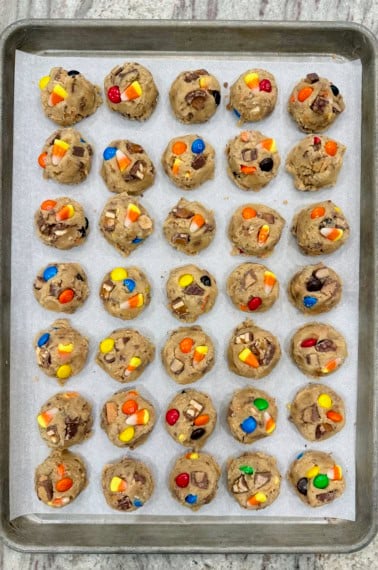 35 cookie dough balls made with leftover Halloween candy on a parchment lined aluminum baking sheet.