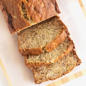 A sliced loaf of banana bread on a parchment lined light wood board.