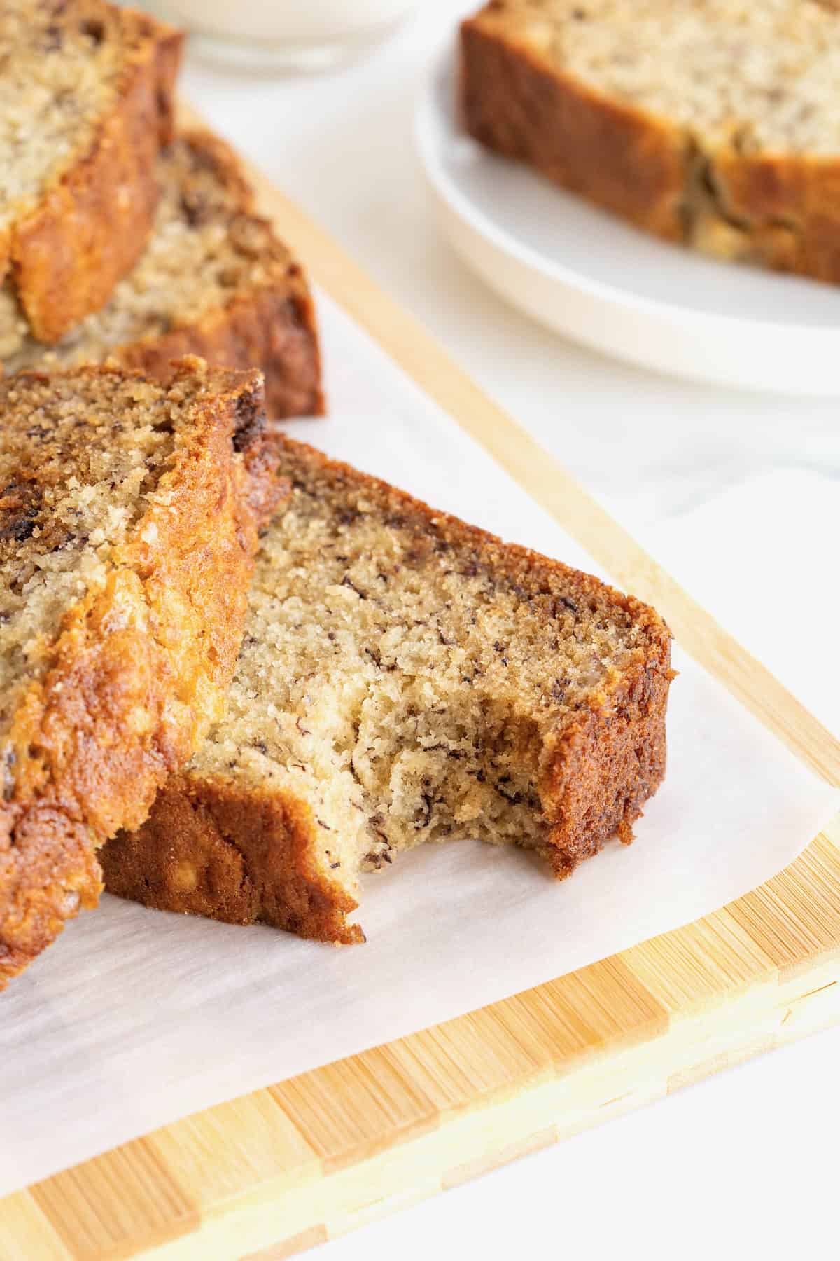 A sliced loaf of banana bread on a parchment lined light wood board. One of the slices has a bite out of it.