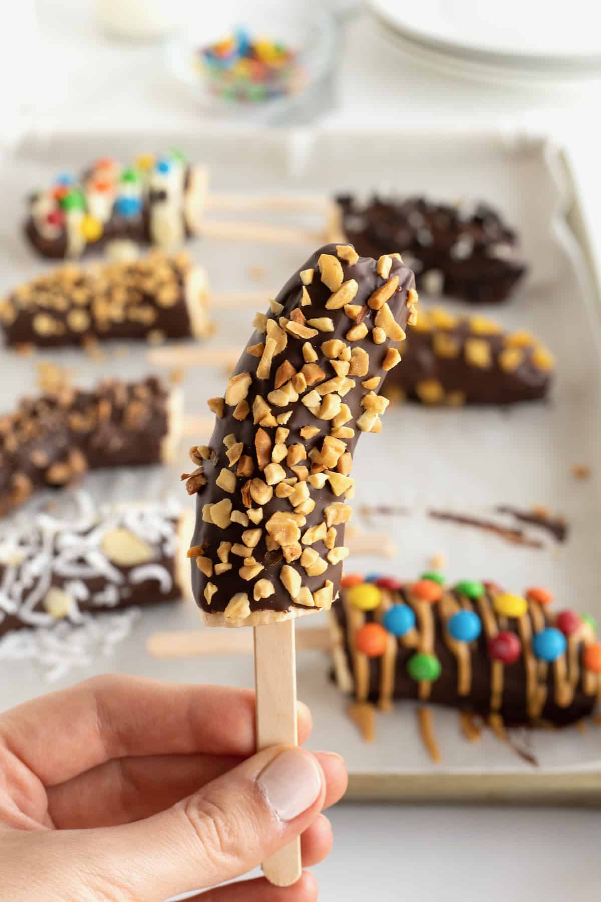A frozen banana on a popsicle stick covered in chocolate and crushed peanuts.