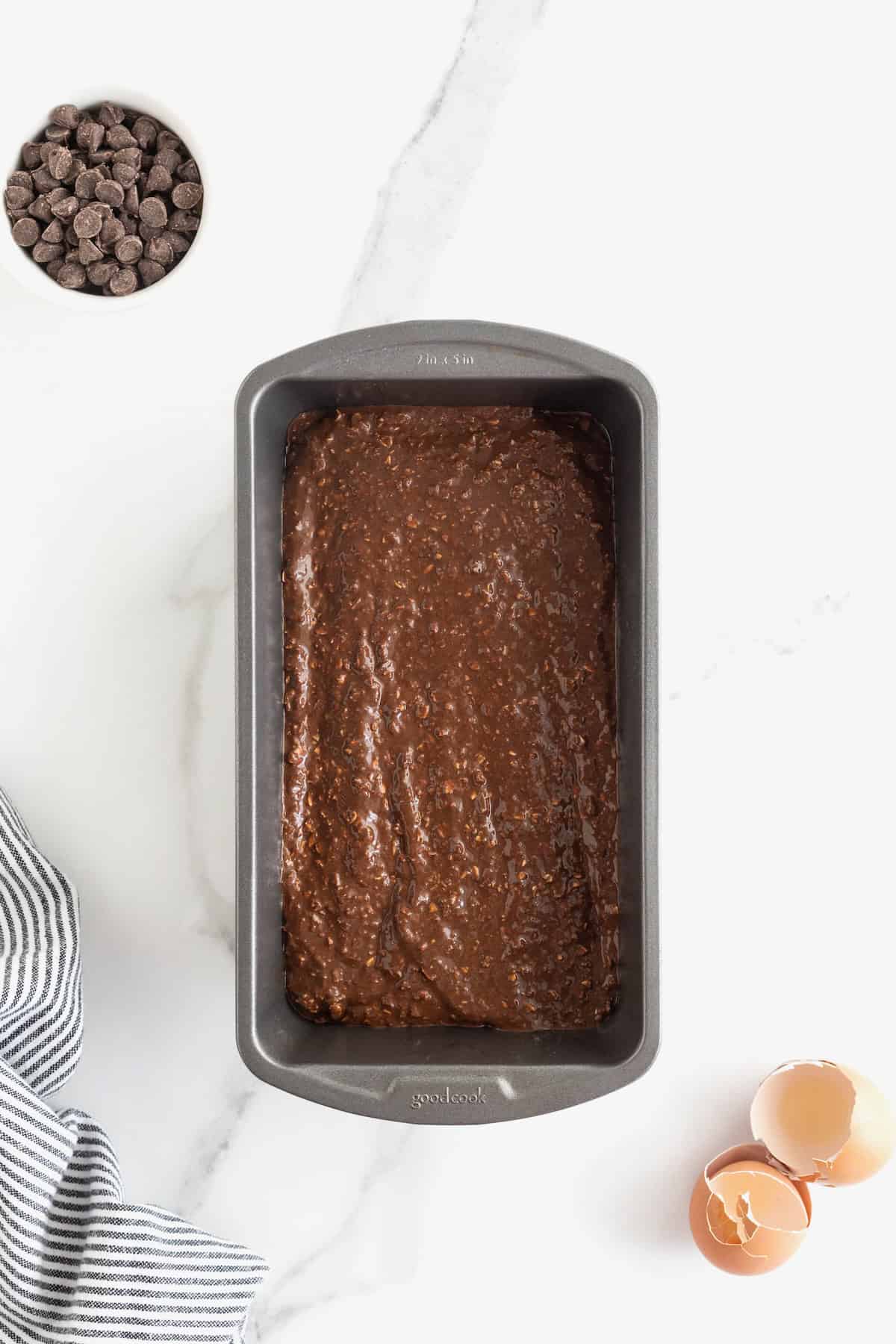 Chocolate banana bread batter in a dark aluminum loaf pan on a white marble counter.
