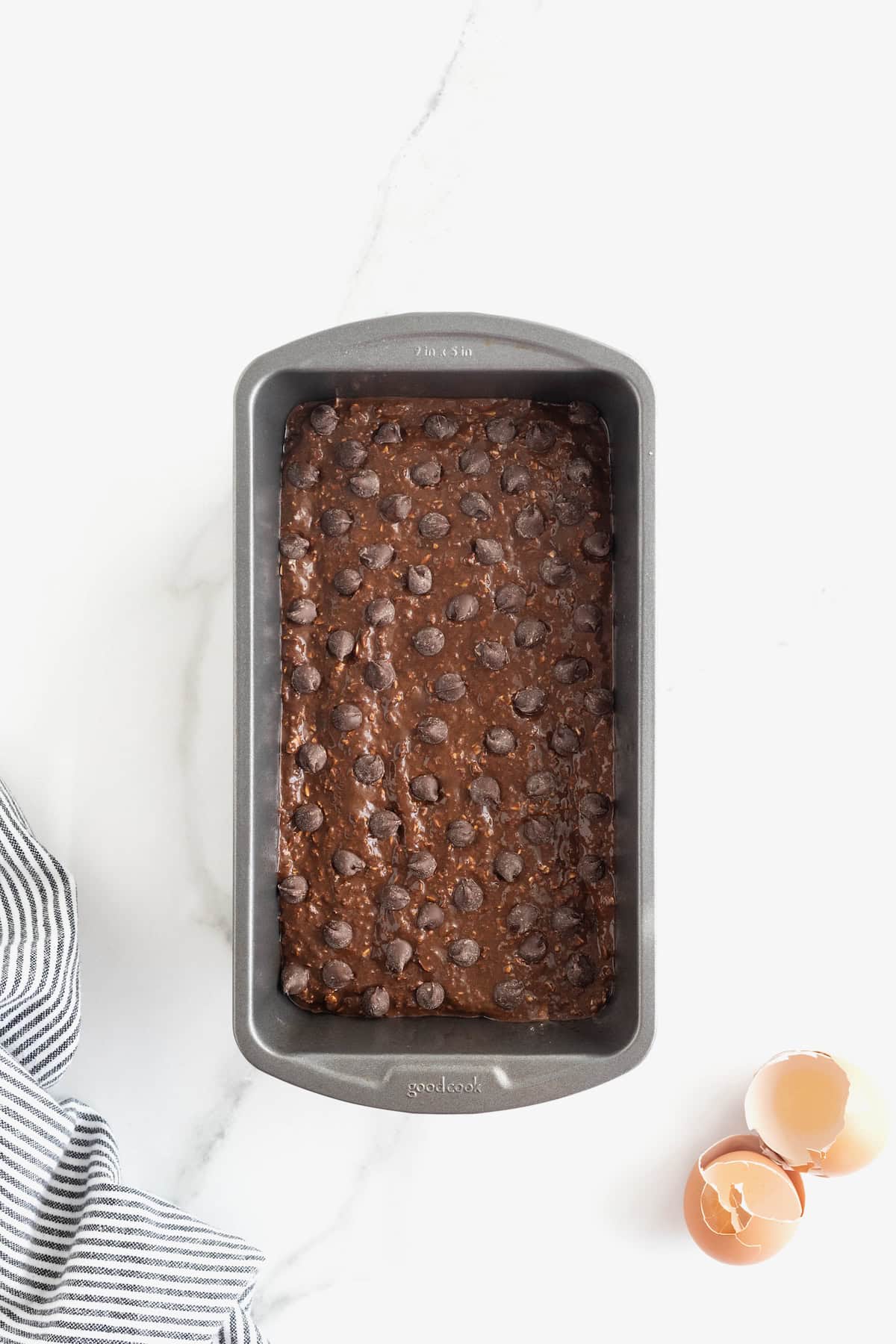 Chocolate banana bread batter topped with chocolate chips in a dark aluminum loaf pan.