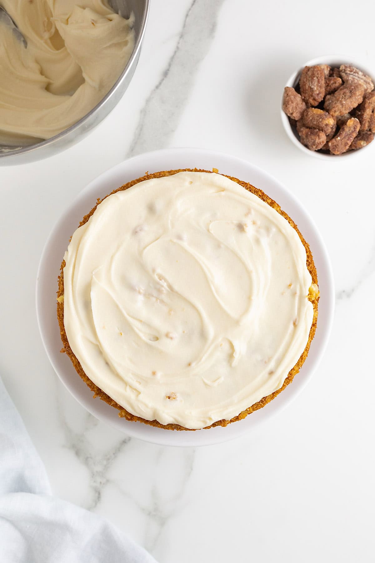 A layer of buttercream icing on a round cake on a white cake stand as seen from above.