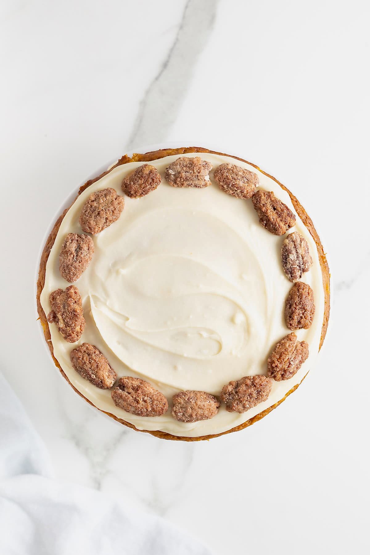 The top of a white frosted cake ringed in candied pecans.