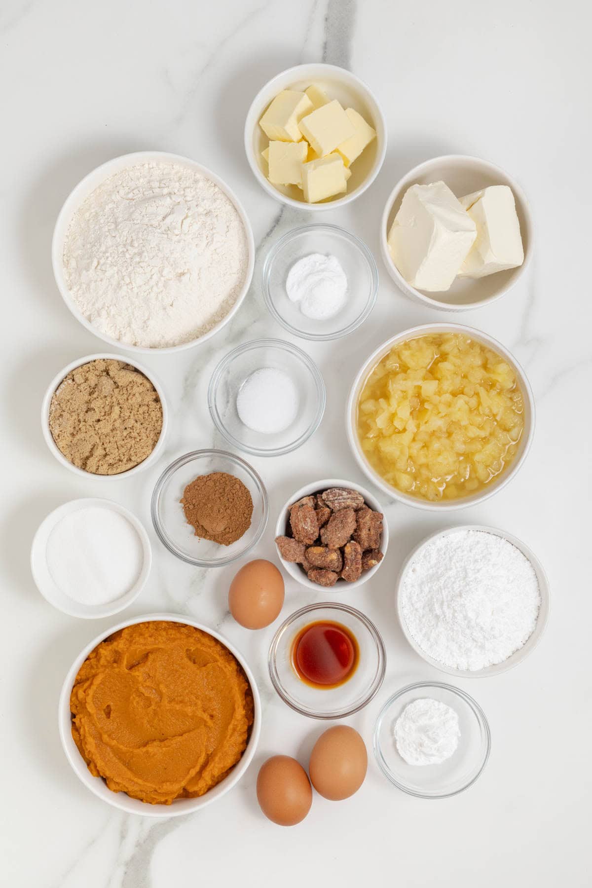 Ingredients to make pumpkin pineapple cake in small glass dishes on a white marble counter.