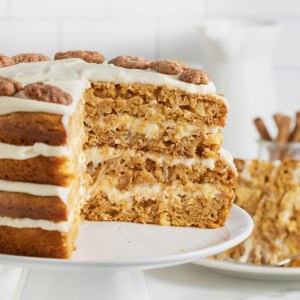A layered pumpkin pineapple cake on a white cake stand. A large wedge is cut out of the cake to reveal the inside layers.