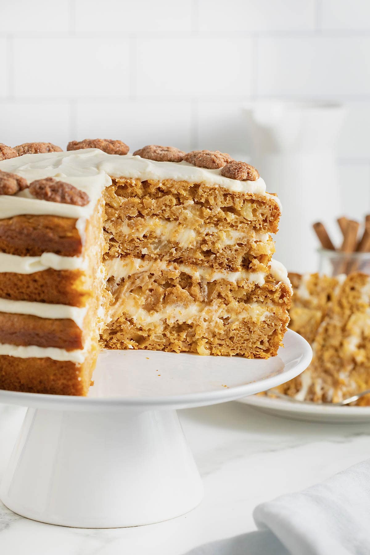 A layered pumpkin pineapple cake on a white cake stand. A large wedge is cut out of the cake to reveal the inside layers.