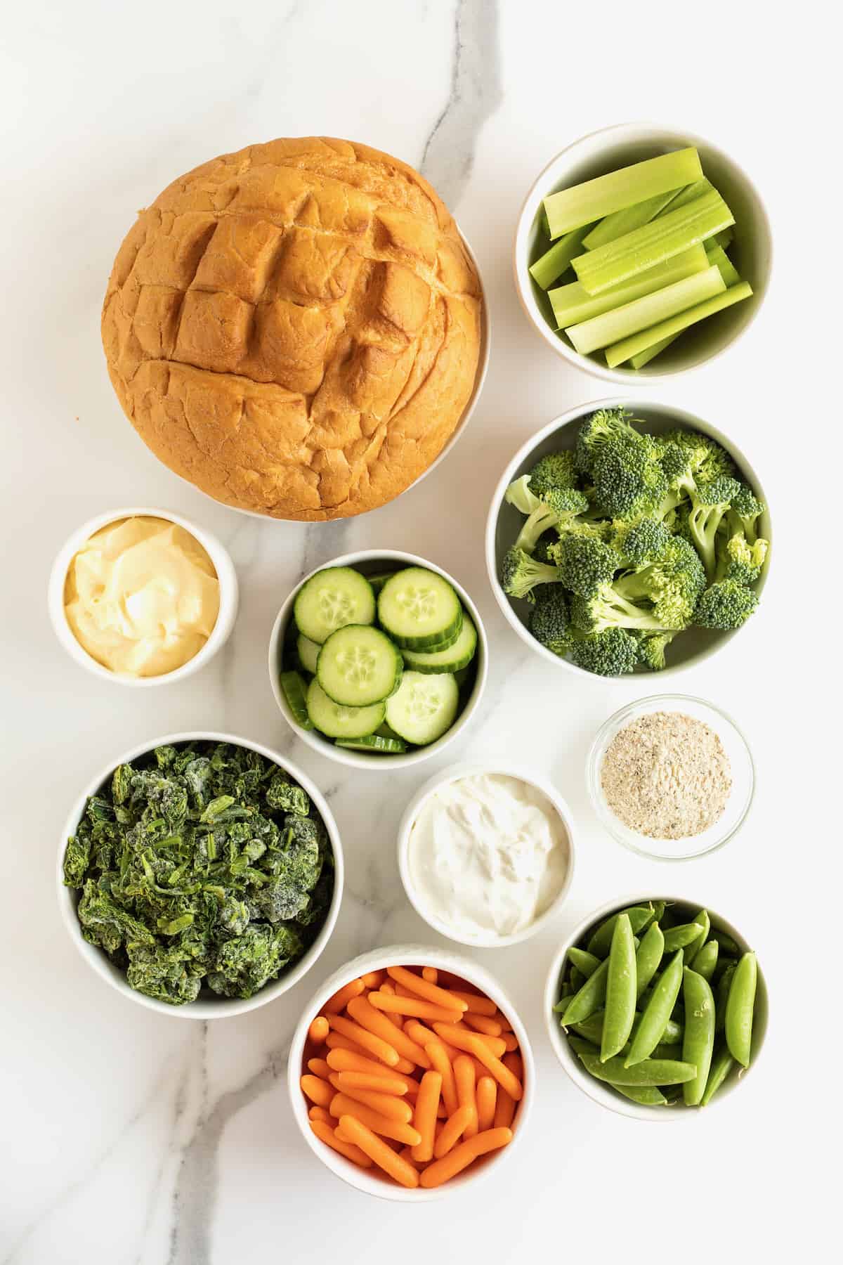 A bread bowl, cucumber slices, broccoli florets, carrot sticks, spinach and cream cheese for a spinach dip.