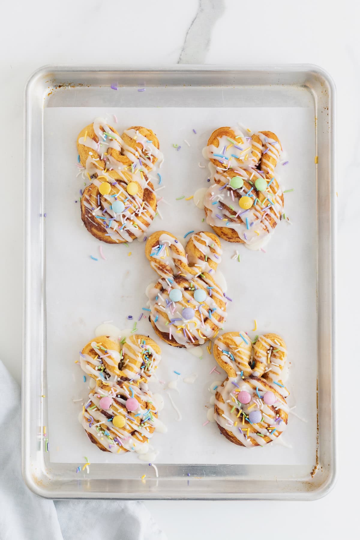 Five Easter Bunny Cinnamon Rolls on a parchment lined aluminum baking sheet.