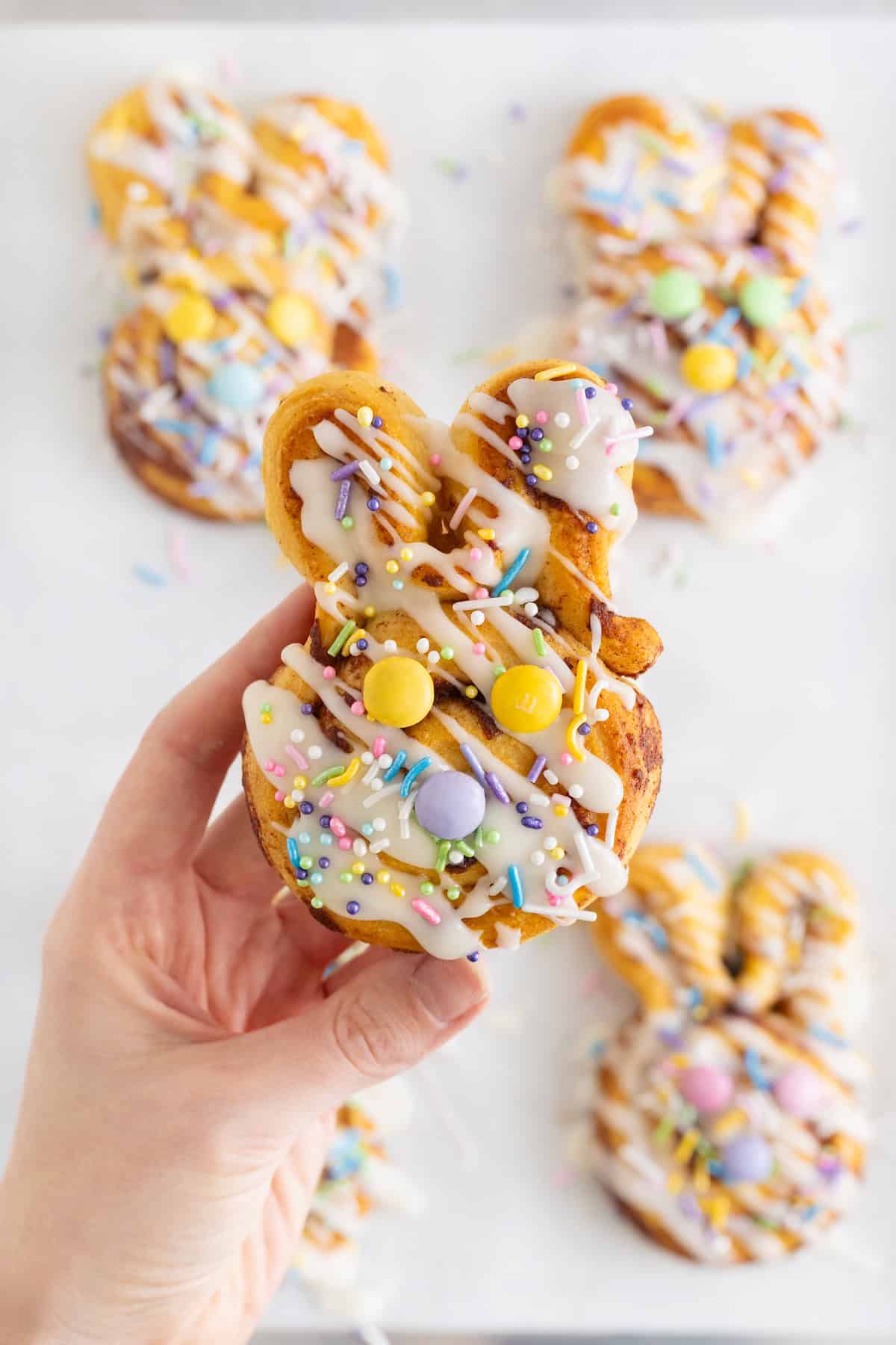A hand holding an easter bunny shaped cinnamon roll decorated with Easter M&Ms.