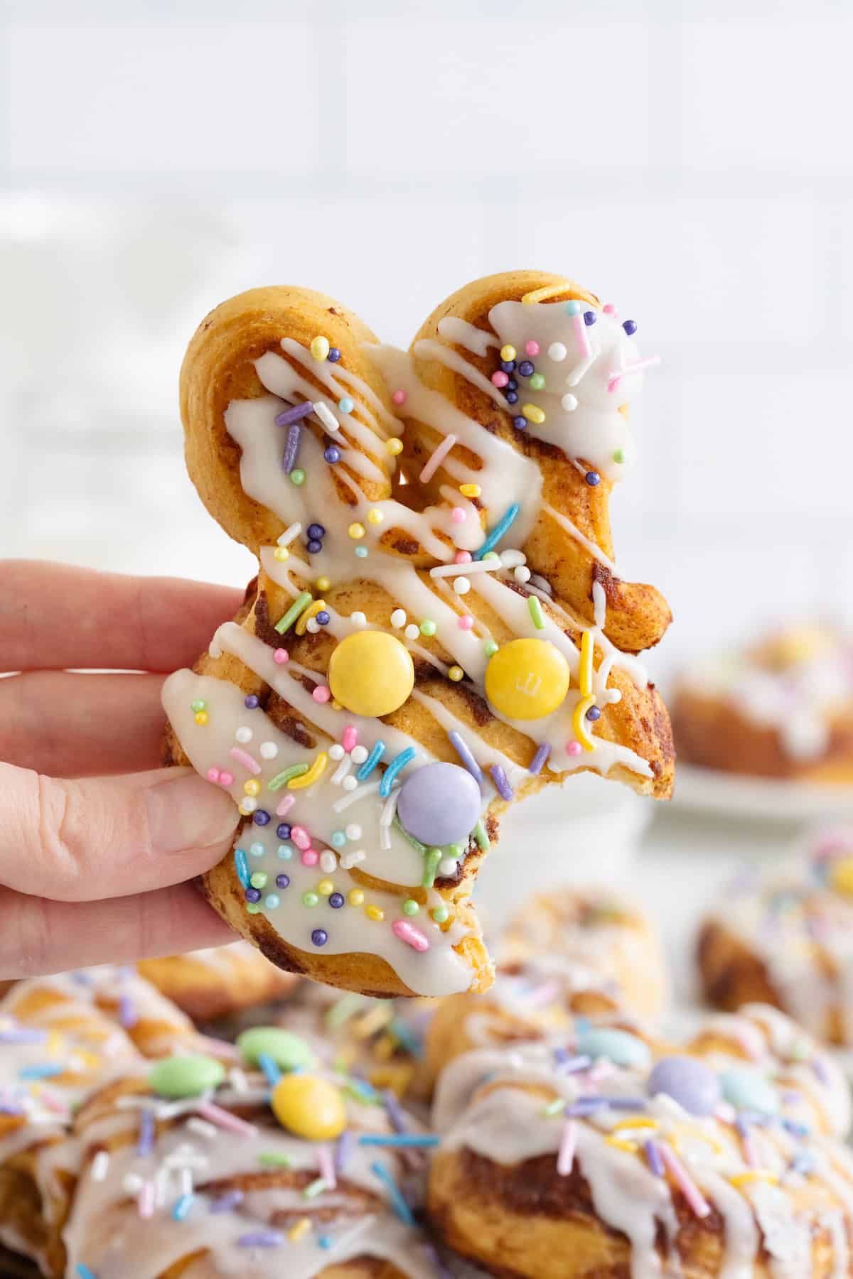 A hand holding an easter bunny shaped cinnamon roll with a bite taken out of it.