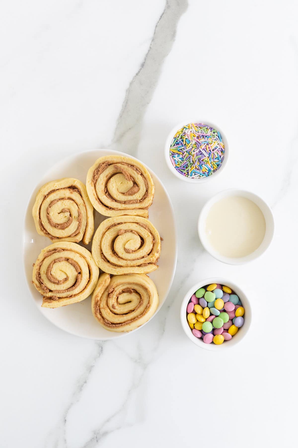 Ingredients to make Easter Bunny Cinnamon Rolls in white dishes on a white marble counter.