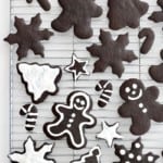 A metal cooling rack with Christmas shaped chocolate cookies of various sizes. Some of the cookies have white icing on them.