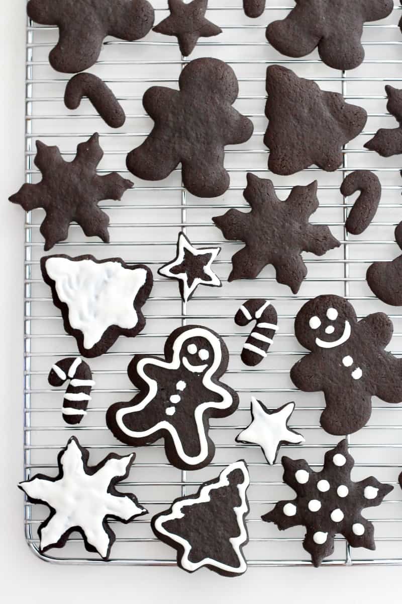 A metal cooling rack with Christmas shaped chocolate cookies of various sizes. Some of the cookies have white icing on them.