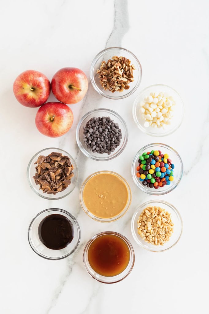 Ingredients to make apple nachos in small glass dishes on a white marble counter.